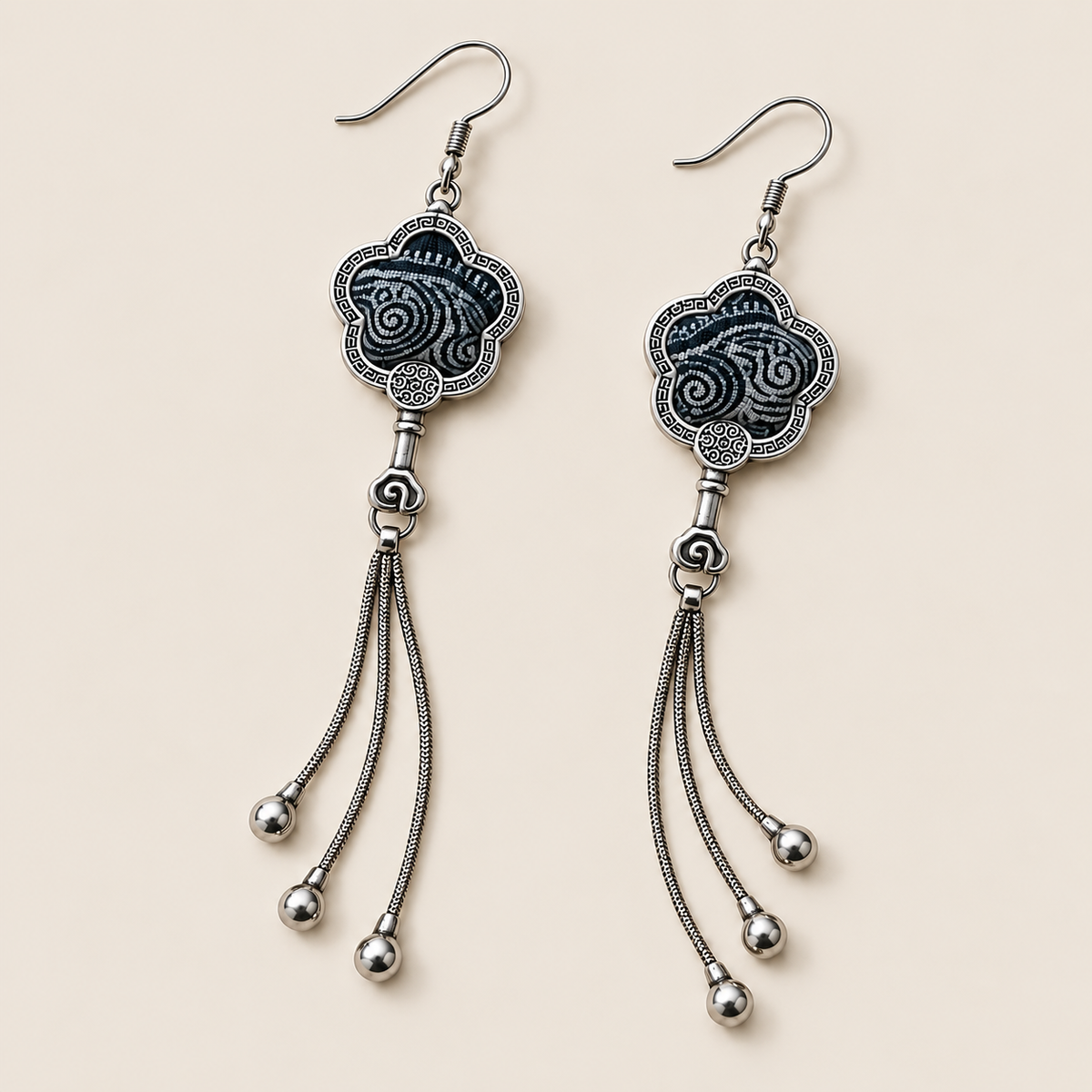 Midnight Blossom floral tassel earrings laid diagonally with deep indigo batik with pale flowing curves facing up and three chain tassels with rounded drops visible.