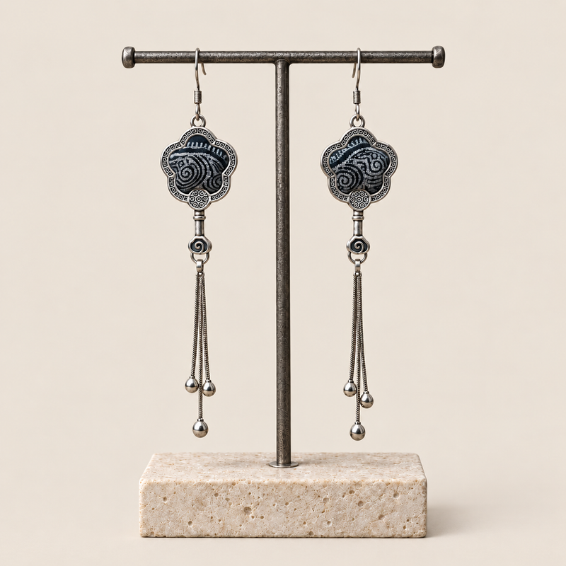 Midnight Blossom floral tassel earrings hanging from a T-bar stand, showing deep indigo batik with pale flowing curves and three chain tassels with rounded drops.