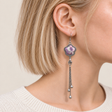 Close-up of Lilac Serenade floral tassel earrings worn with lilac and pink petals with pale curved lines facing outward.
