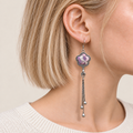 Close-up of Lilac Serenade floral tassel earrings worn with lilac and pink petals with pale curved lines facing outward.