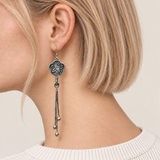 Close-up of Lilac Serenade floral tassel earrings worn with the bird-and-branch metal relief reverse facing outward.
