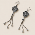 Lilac Serenade floral tassel earrings laid diagonally with bird-and-branch relief backs facing up and three chain tassels with rounded drops visible.