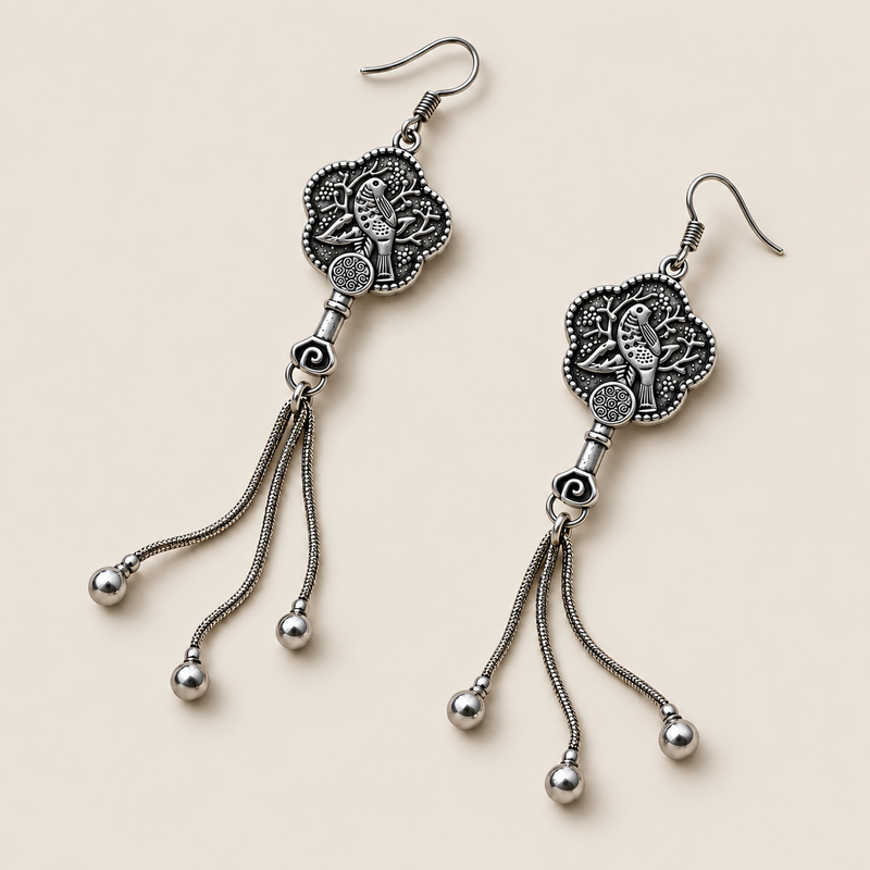 Lilac Serenade floral tassel earrings laid diagonally with bird-and-branch relief backs facing up and three chain tassels with rounded drops visible.