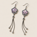 Lilac Serenade floral tassel earrings laid diagonally with lilac and pink petals with pale curved lines facing up and three chain tassels with rounded drops visible.