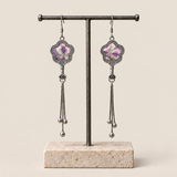 Lilac Serenade floral tassel earrings hanging from a T-bar stand, showing lilac and pink petals with pale curved lines and three chain tassels with rounded drops.
