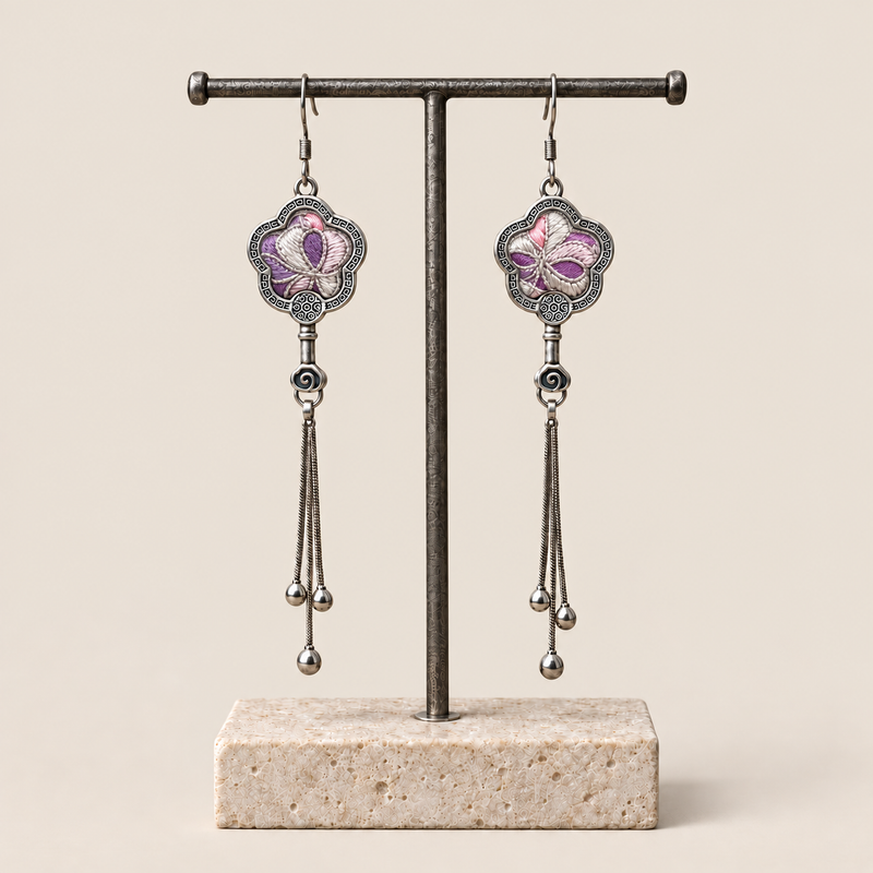 Lilac Serenade floral tassel earrings hanging from a T-bar stand, showing lilac and pink petals with pale curved lines and three chain tassels with rounded drops.