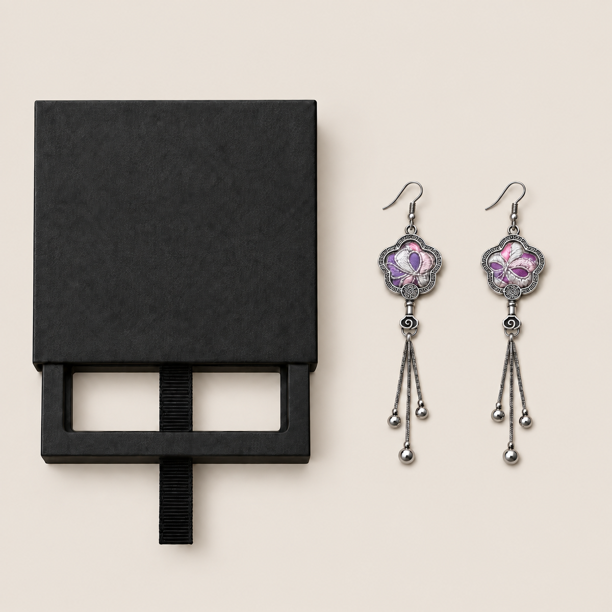 Black drawer-style box pictured beside Lilac Serenade floral tassel earrings, with textile fronts and metal relief backs visible.