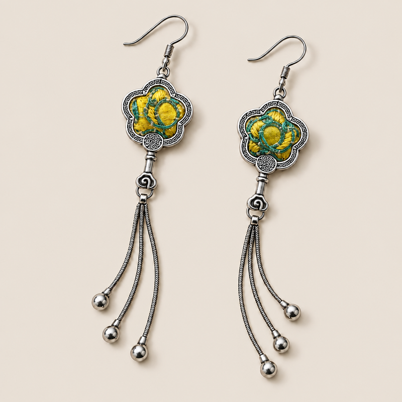 Golden Meadow floral tassel earrings laid diagonally with yellow and green floral embroidery facing up and three chain tassels with rounded drops visible.