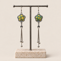 Golden Meadow floral tassel earrings hanging from a T-bar stand, showing yellow and green floral embroidery and three chain tassels with rounded drops.