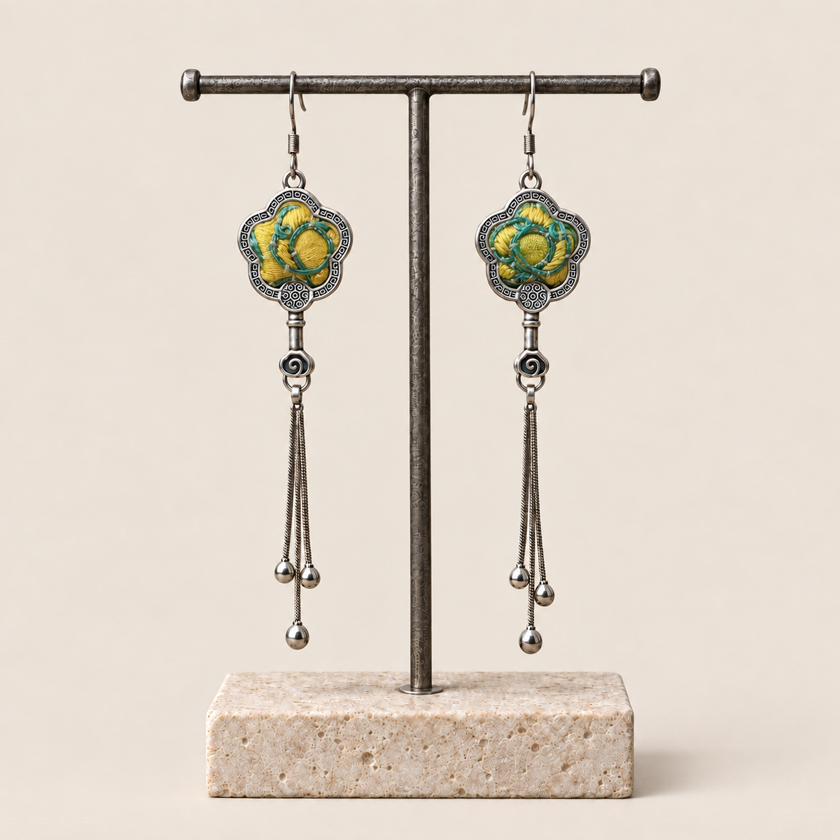 Golden Meadow floral tassel earrings hanging from a T-bar stand, showing yellow and green floral embroidery and three chain tassels with rounded drops.