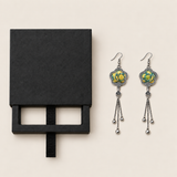 Black drawer-style box pictured beside Golden Meadow floral tassel earrings, with textile fronts and metal relief backs visible.