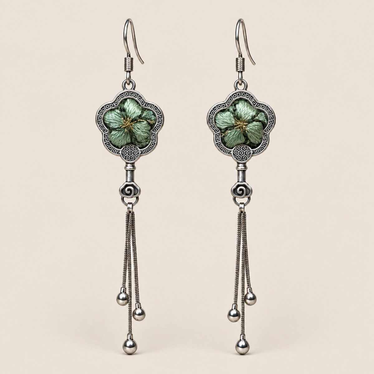 Jade Whisper floral tassel earrings, front view showing soft green floral embroidery in flower-shaped metal frames with three chain tassels with rounded drops.