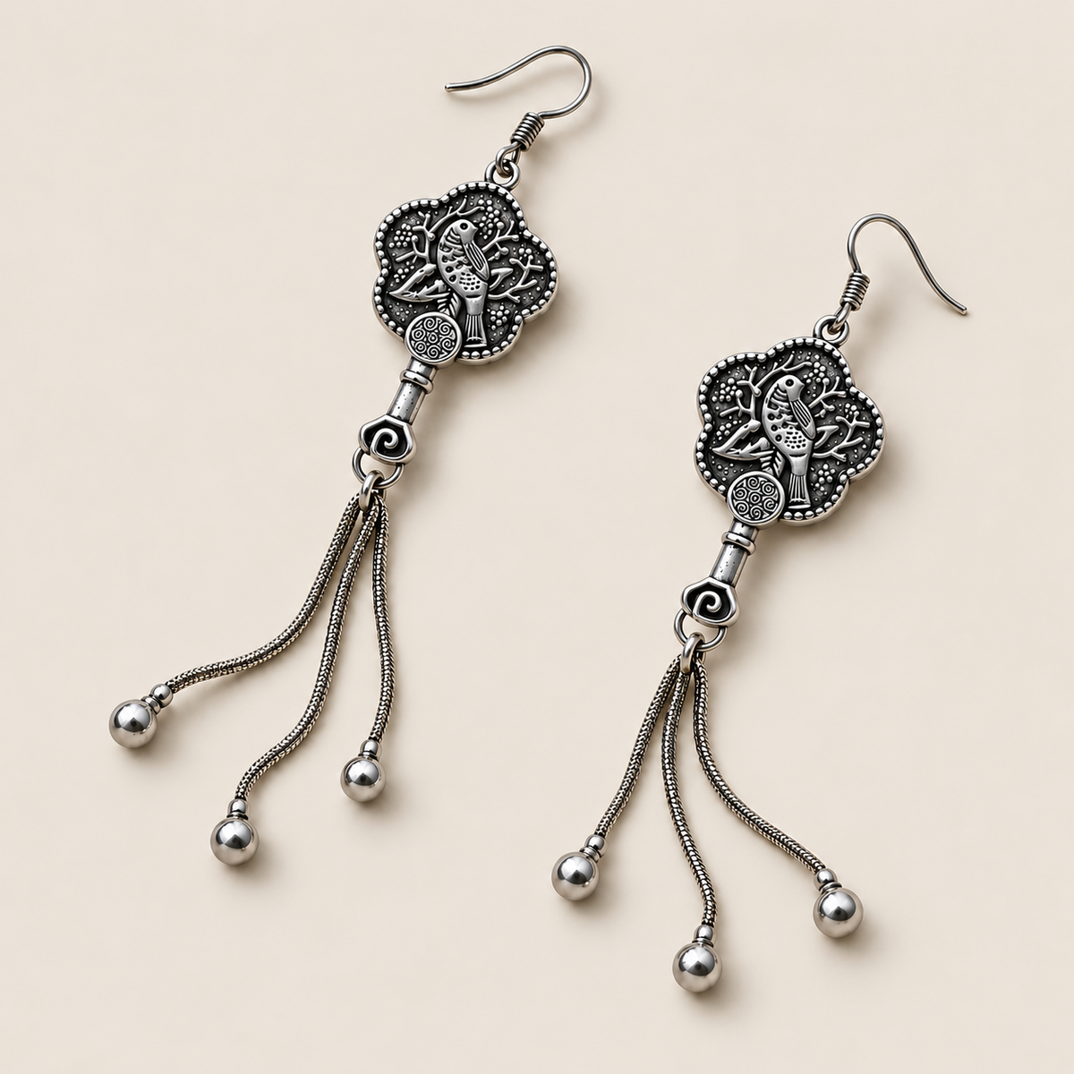 Jade Whisper floral tassel earrings laid diagonally with bird-and-branch relief backs facing up and three chain tassels with rounded drops visible.