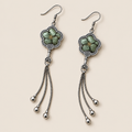 Jade Whisper floral tassel earrings laid diagonally with soft green floral embroidery facing up and three chain tassels with rounded drops visible.