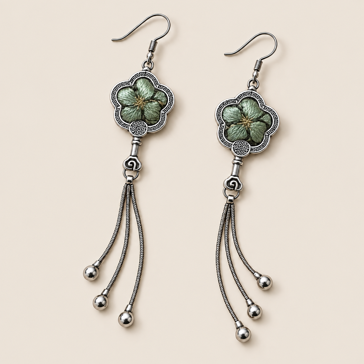 Jade Whisper floral tassel earrings laid diagonally with soft green floral embroidery facing up and three chain tassels with rounded drops visible.