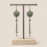 Jade Whisper floral tassel earrings hanging from a T-bar stand, showing soft green floral embroidery and three chain tassels with rounded drops.