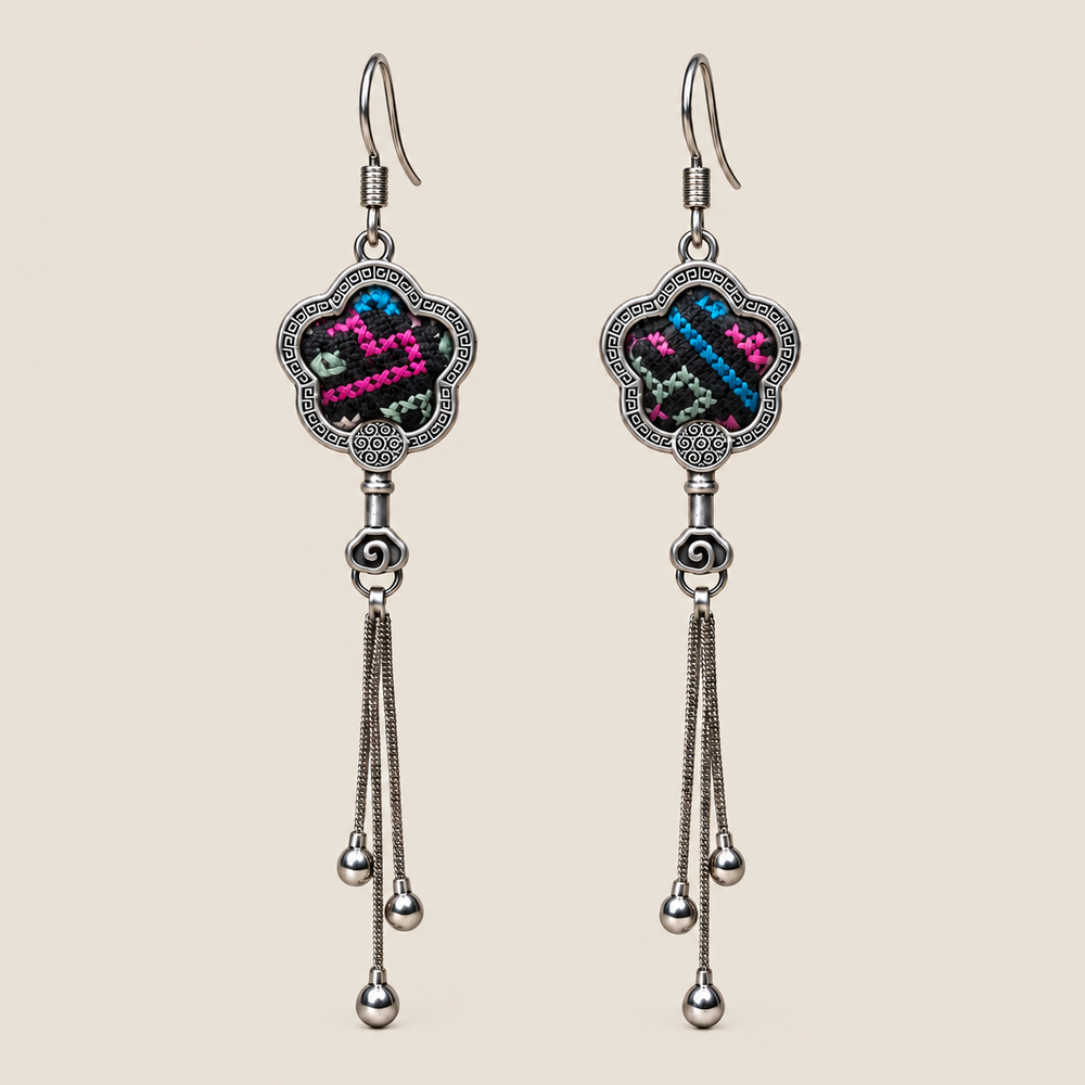 Rose Constellation floral tassel earrings, front view showing pink, green and blue geometric stitches on a dark ground in flower-shaped metal frames with three chain tassels with rounded drops.