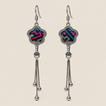 Rose Constellation floral tassel earrings, front view showing pink, green and blue geometric stitches on a dark ground in flower-shaped metal frames with three chain tassels with rounded drops.