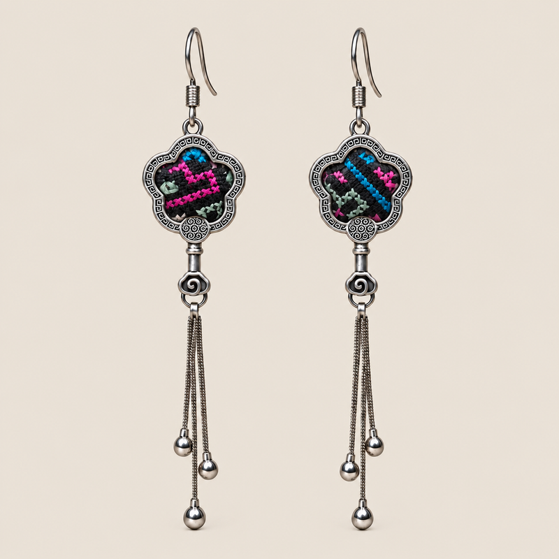 Rose Constellation floral tassel earrings, front view showing pink, green and blue geometric stitches on a dark ground in flower-shaped metal frames with three chain tassels with rounded drops.