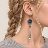 Close-up of Rose Constellation floral tassel earrings worn with pink, green and blue geometric stitches on a dark ground facing outward.