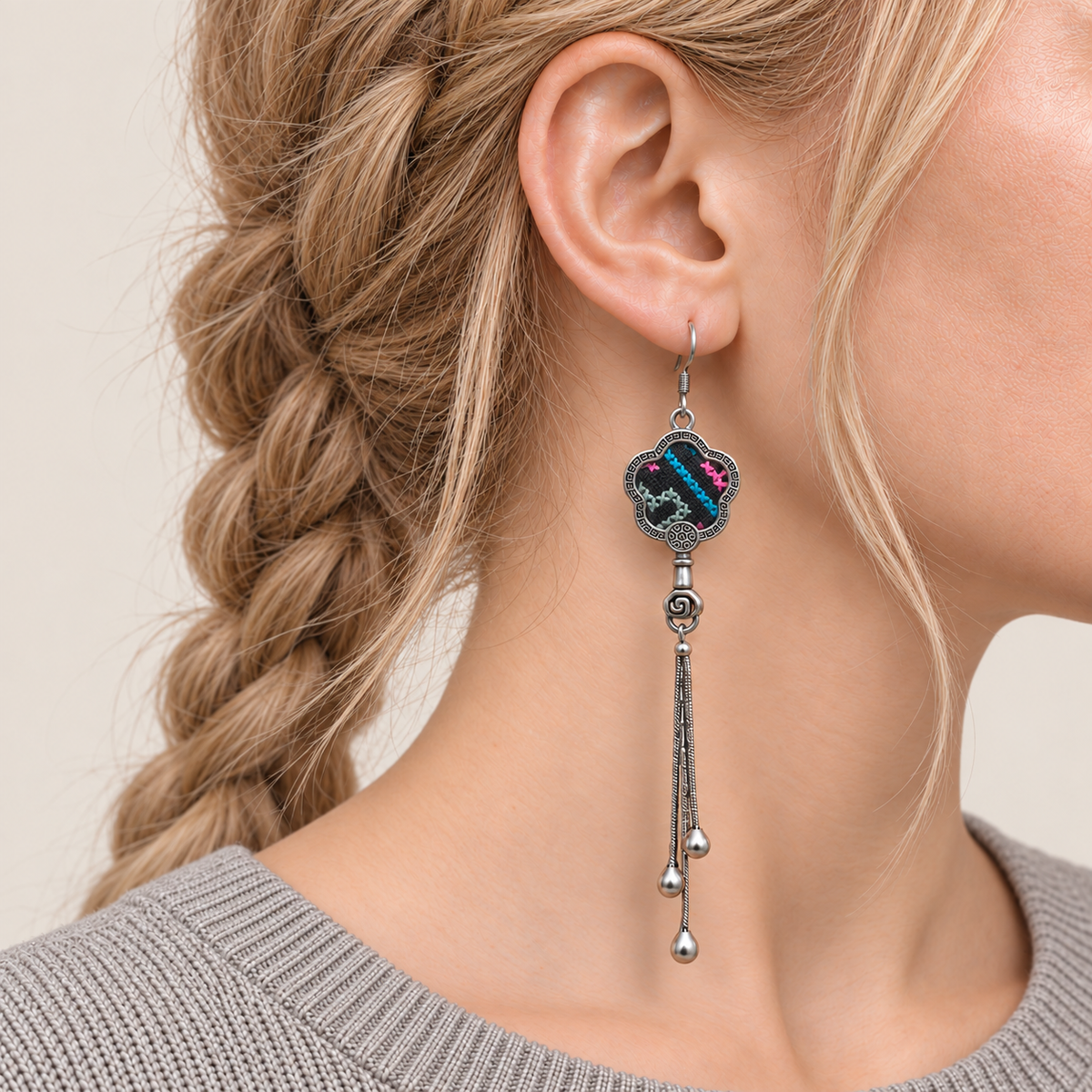 Close-up of Rose Constellation floral tassel earrings worn with pink, green and blue geometric stitches on a dark ground facing outward.