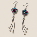 Rose Constellation floral tassel earrings laid diagonally with pink, green and blue geometric stitches on a dark ground facing up and three chain tassels with rounded drops visible.