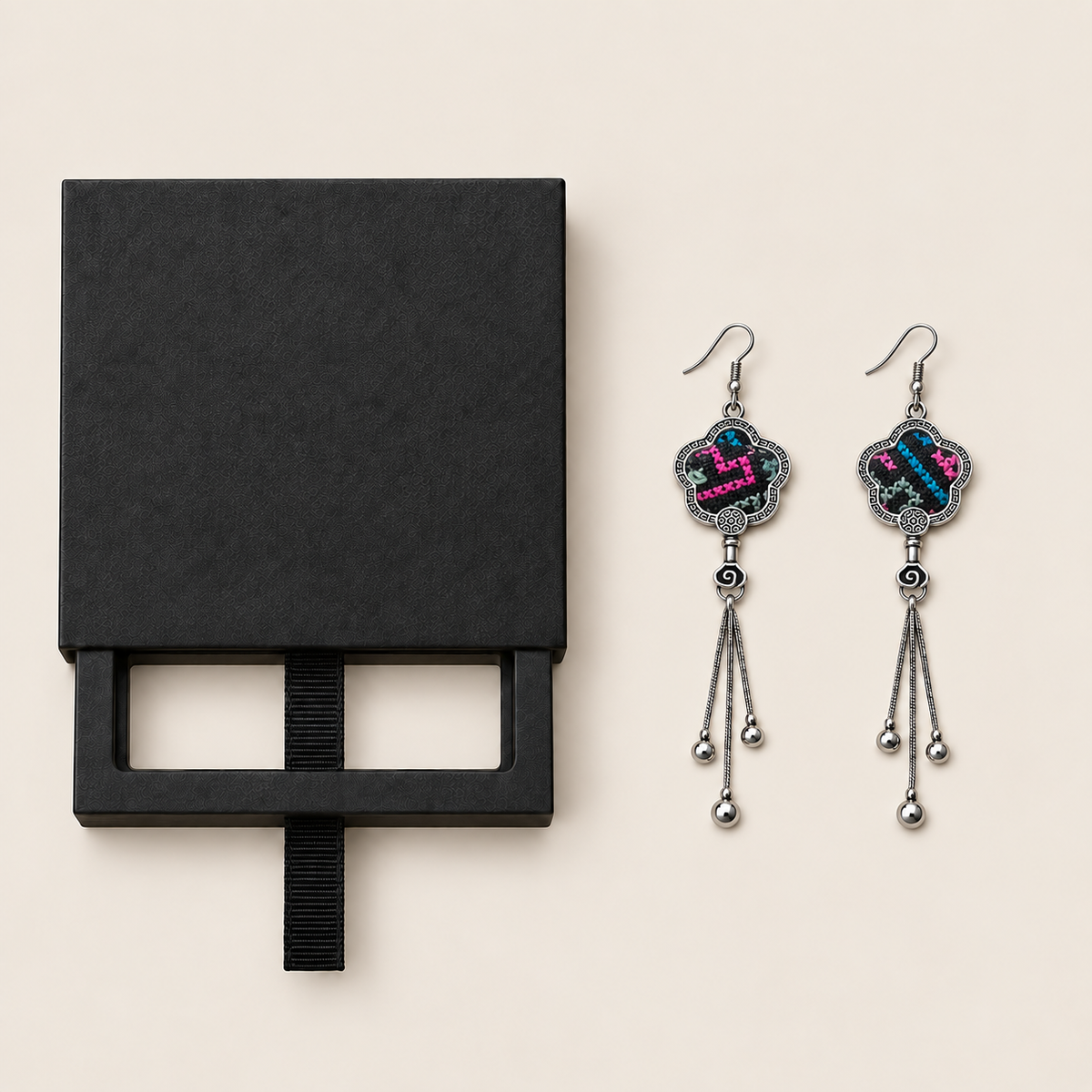 Black drawer-style box pictured beside Rose Constellation floral tassel earrings, with textile fronts and metal relief backs visible.