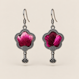 Fuchsia Dawn floral earrings, front view showing radiating fuchsia and rose-pink petals on a dark ground in flower-shaped metal frames with small spiral drops.