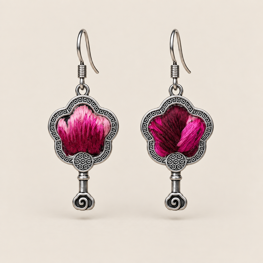Fuchsia Dawn floral earrings, front view showing radiating fuchsia and rose-pink petals on a dark ground in flower-shaped metal frames with small spiral drops.