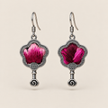 Fuchsia Dawn floral earrings, front view showing radiating fuchsia and rose-pink petals on a dark ground in flower-shaped metal frames with small spiral drops.