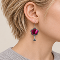 Close-up of Fuchsia Dawn floral earrings worn with radiating fuchsia and rose-pink petals on a dark ground facing outward.