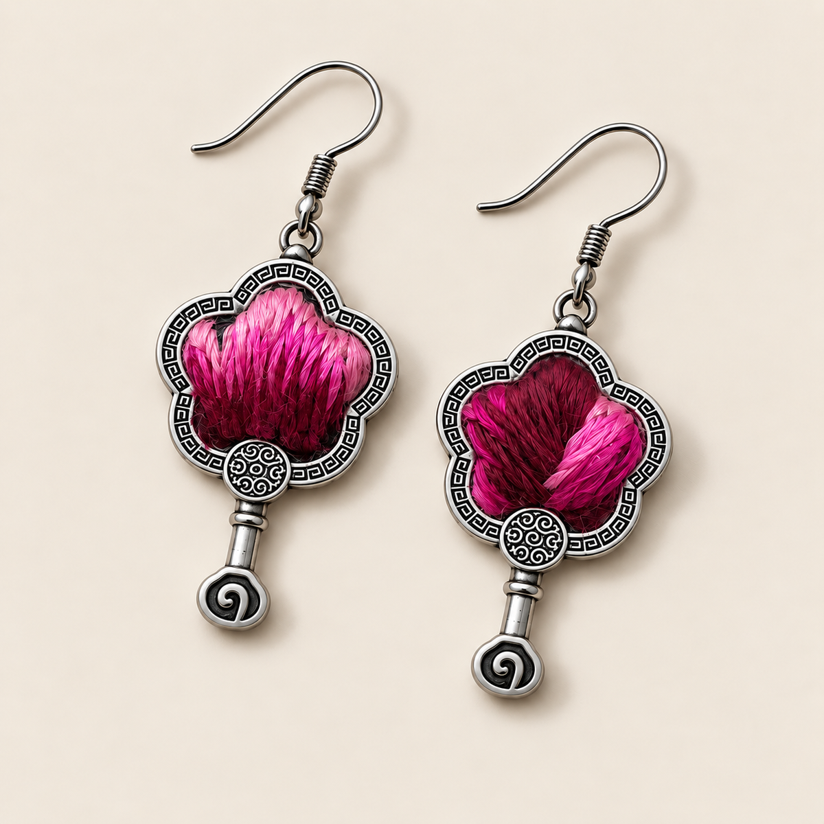 Fuchsia Dawn floral earrings laid diagonally with radiating fuchsia and rose-pink petals on a dark ground facing up and small spiral drops visible.