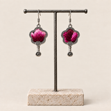 Fuchsia Dawn floral earrings hanging from a T-bar stand, showing radiating fuchsia and rose-pink petals on a dark ground and small spiral drops.