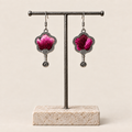 Fuchsia Dawn floral earrings hanging from a T-bar stand, showing radiating fuchsia and rose-pink petals on a dark ground and small spiral drops.