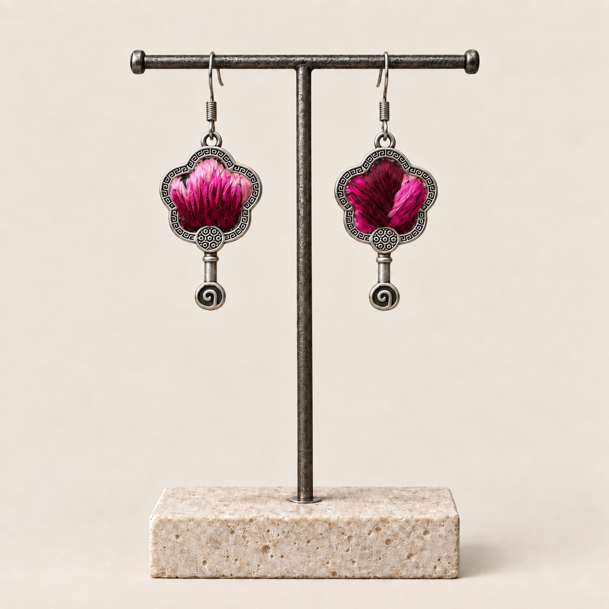 Fuchsia Dawn floral earrings hanging from a T-bar stand, showing radiating fuchsia and rose-pink petals on a dark ground and small spiral drops.