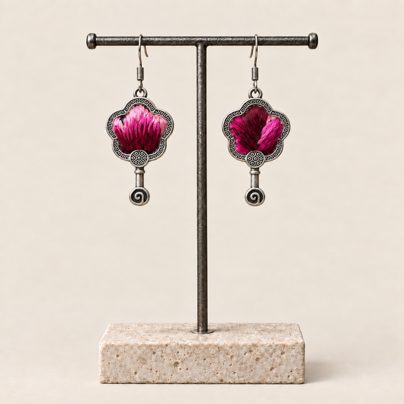 Fuchsia Dawn floral earrings hanging from a T-bar stand, showing radiating fuchsia and rose-pink petals on a dark ground and small spiral drops.