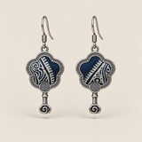 Indigo Echo floral earrings, front view showing pale geometric lines on deep indigo batik in flower-shaped metal frames with small spiral drops.