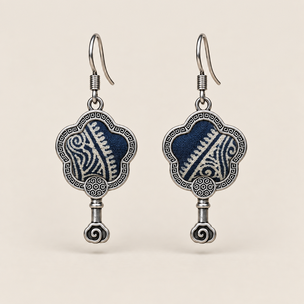 Indigo Echo floral earrings, front view showing pale geometric lines on deep indigo batik in flower-shaped metal frames with small spiral drops.