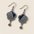 Indigo Echo floral earrings laid diagonally with pale geometric lines on deep indigo batik facing up and small spiral drops visible.