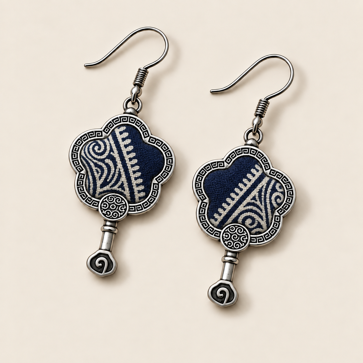 Indigo Echo floral earrings laid diagonally with pale geometric lines on deep indigo batik facing up and small spiral drops visible.