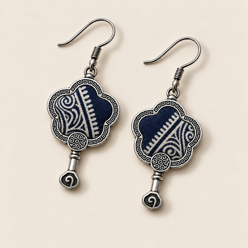 Indigo Echo floral earrings laid diagonally with pale geometric lines on deep indigo batik facing up and small spiral drops visible.