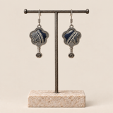 Indigo Echo floral earrings hanging from a T-bar stand, showing pale geometric lines on deep indigo batik and small spiral drops.