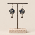 Indigo Echo floral earrings hanging from a T-bar stand, showing pale geometric lines on deep indigo batik and small spiral drops.