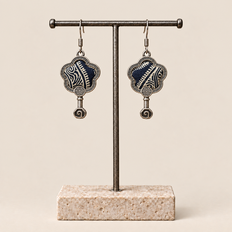 Indigo Echo floral earrings hanging from a T-bar stand, showing pale geometric lines on deep indigo batik and small spiral drops.