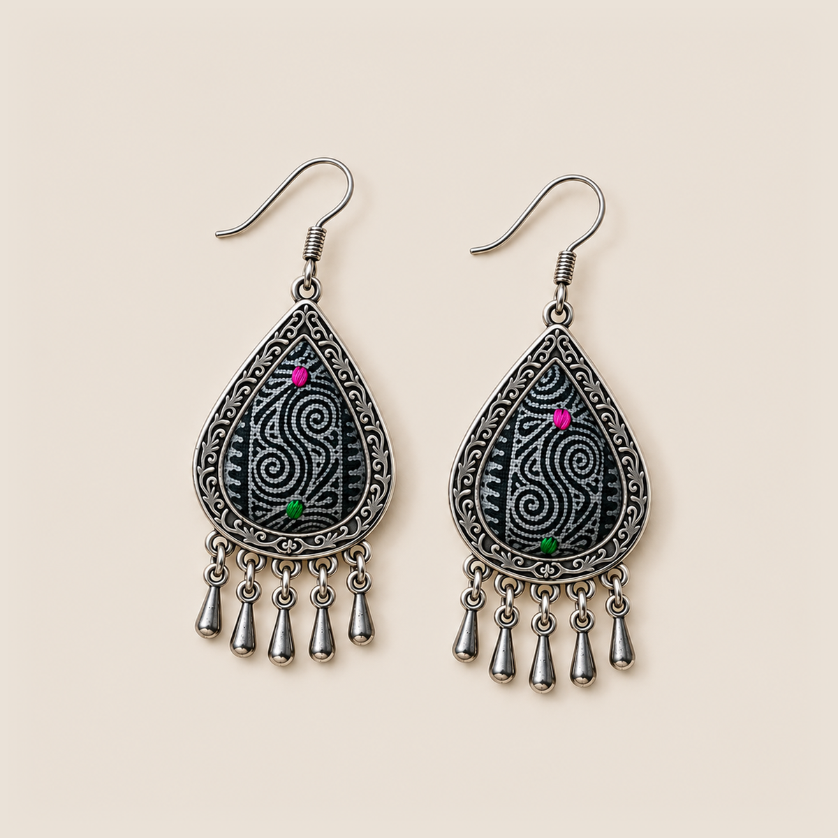 Midnight Currents earrings lying face up, showing differing pale spiral patterns on dark batik textile with pink and green accents.