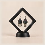 Midnight Currents earrings displayed inside a clear diamond-shaped frame with a black border and base.