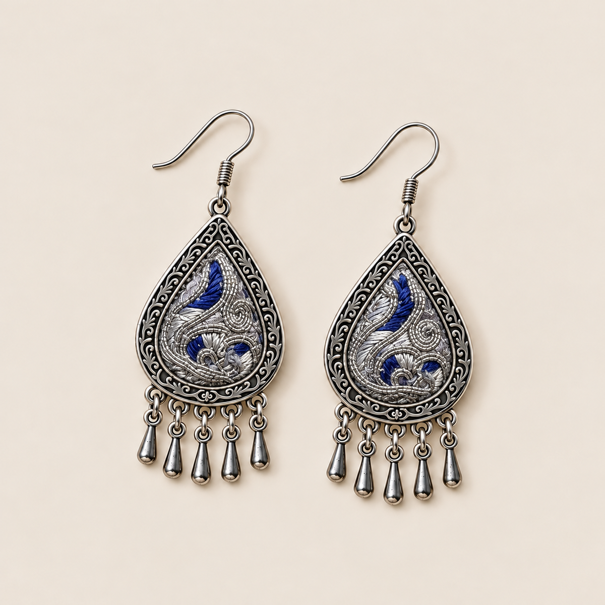 Angled front view of Silver Tide earrings showing silver-toned embroidery curves over deep blue.