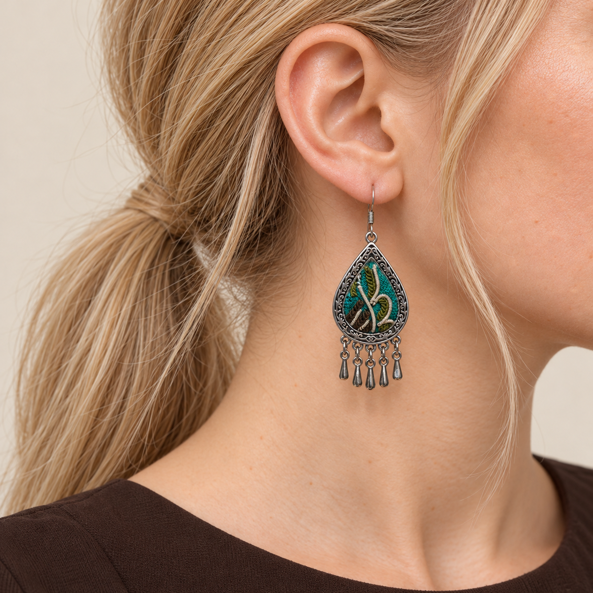 Close-up of a Verdant Reverie earring worn with teal and olive-green embroidery and raised cream curves facing outward.