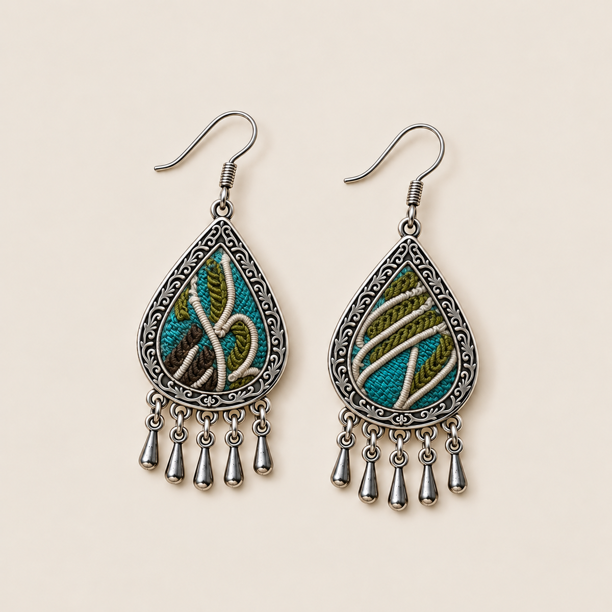 Verdant Reverie earrings laid flat, showing different cream embroidered curves across teal, olive-green and brown textile fronts.