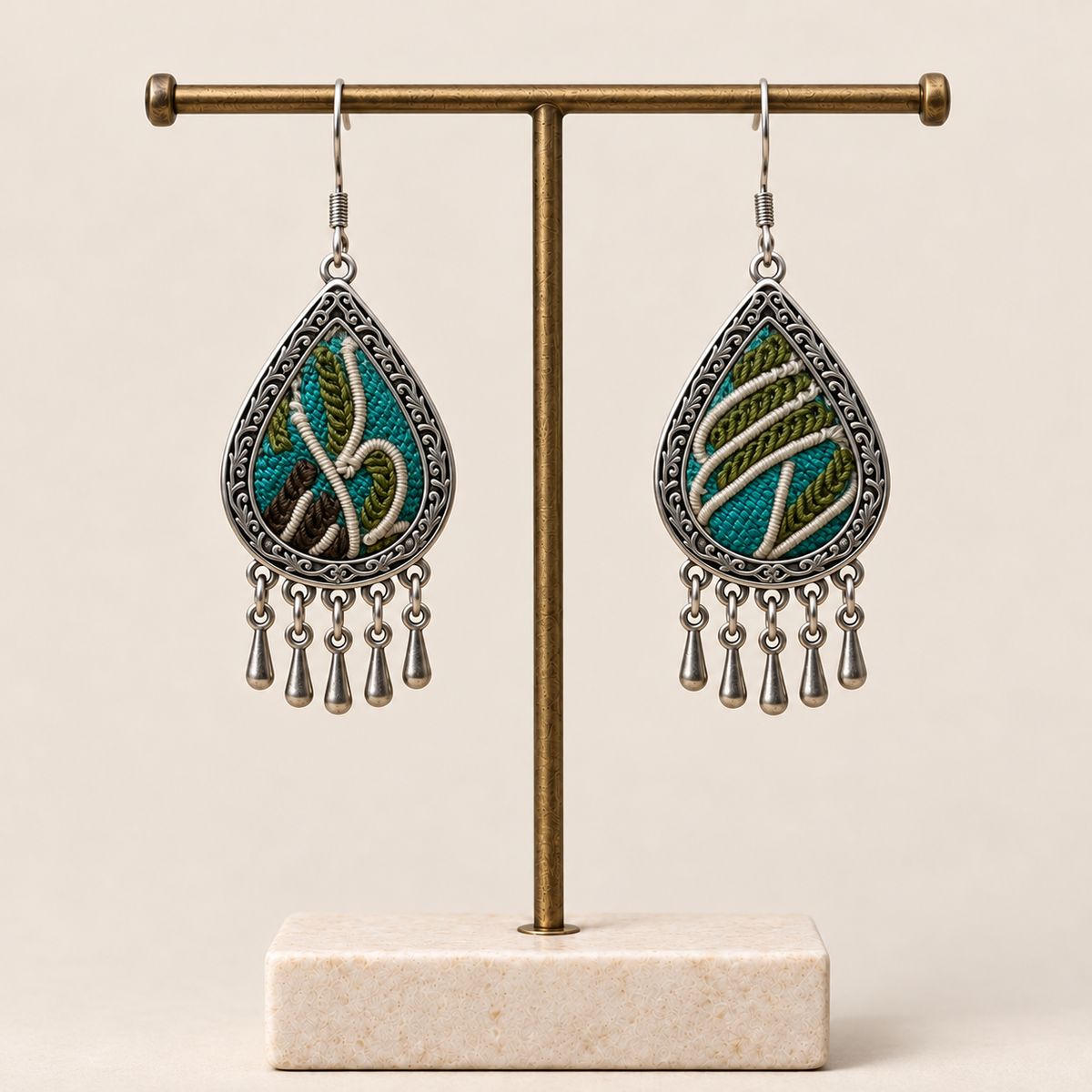 Verdant Reverie embroidered teardrop earrings hanging from a T-bar stand, with five short drops on each earring.